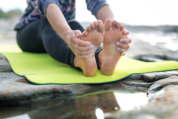 Athletic Woman Stretching on a Yoga Mat on a Rocky Beach