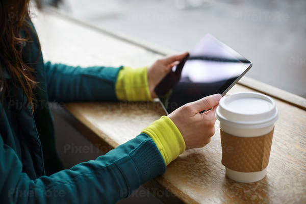 Woman Holding a Tablet Next to the Cup of Coffee at a Shop