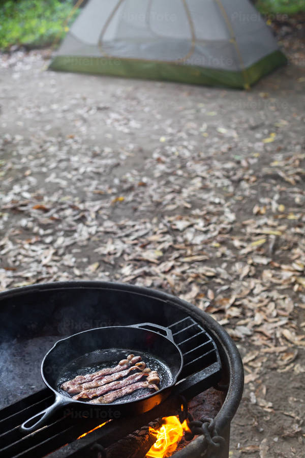 An Iron Skillet with Sizzling Bacon on a Fire Pit in a Campground