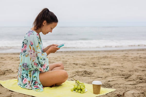 Young Woman Sitting on a Beach and Browsing on a Smartphone