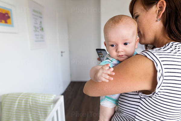 Mom Holding a Baby Boy at Home and Using a Cell Phone
