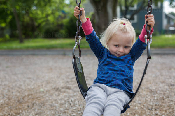 Little Girl Sitting on a Swing at Playground