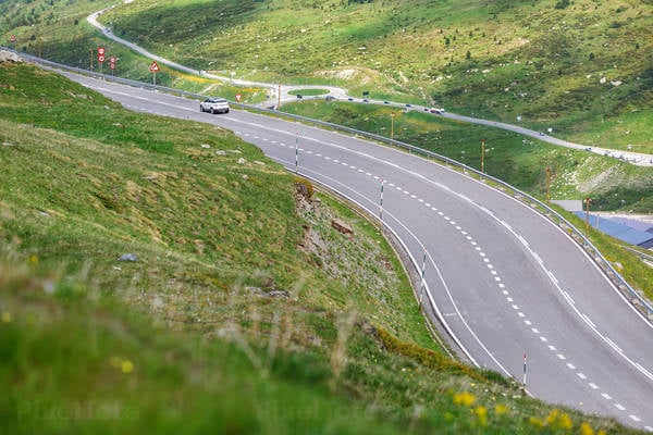 Car Driving on a Mountain Plateau Road with a Roundabout in the Background