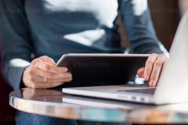 Low-Angle View of a Woman Holding a Digital Tablet While Typing on a Laptop Keyboard