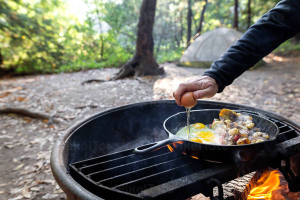 Man Cracking an Egg into an Iron Skillet on an Outdoor Fire Pit