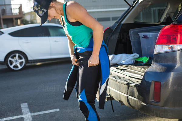 Young Smiling Woman Putting a Wetsuit on Next to a Car