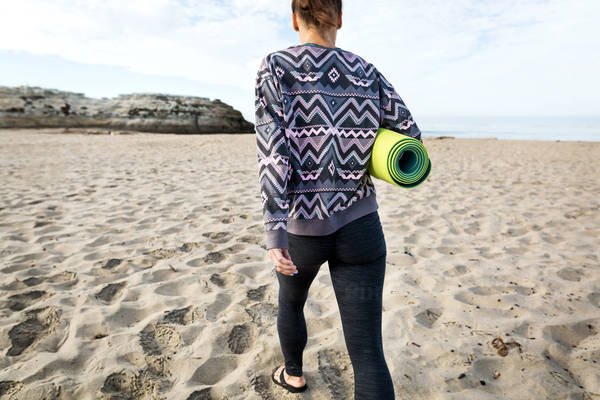 Young Woman with a Yoga Mat Walking on a Beach