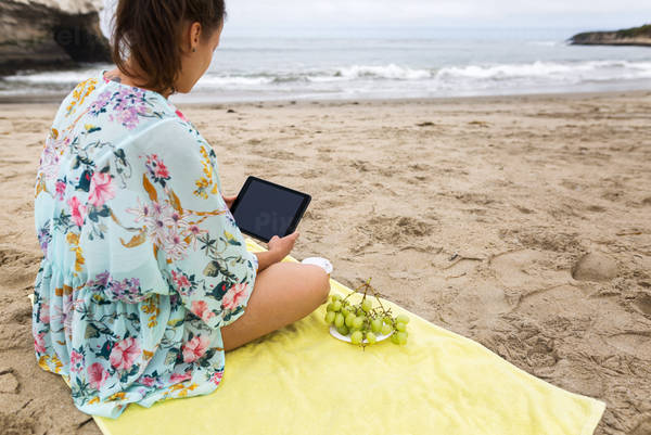 Young Woman Sitting on a Beach Towel and Holding a Tablet