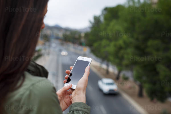 Woman Using a Cell Phone Standing on a Bridge with a Road Below