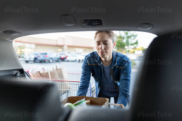 Woman Loading a Shopping Bag with Groceries in a Hatchback Car
