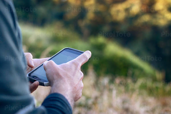 Man Scrolling His Smart Phone with Foliage in the Background