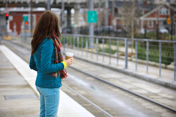 Woman Holding a Cup of Coffee Waiting for a Train at a Public Transportation Platform