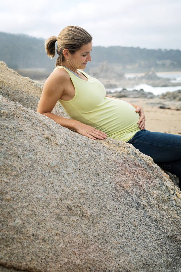 Smiling Pregnant Woman on a Beach Looking at Her Belly