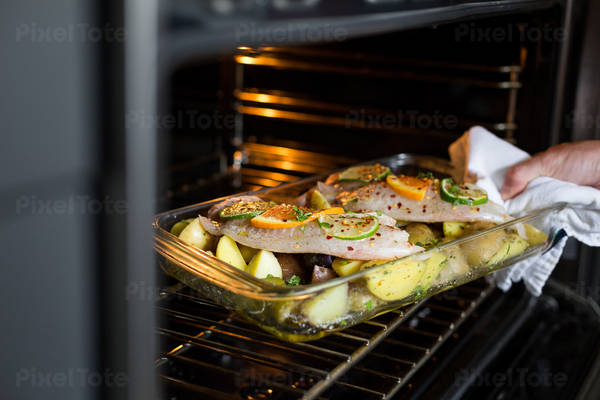 Men Placing a Baking Dish with Fish and Potatoes in an Oven