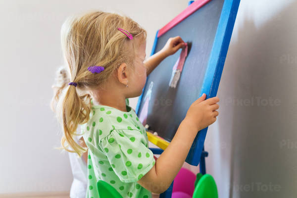 Two Little Girls Drawing on a Chalkboard at Home