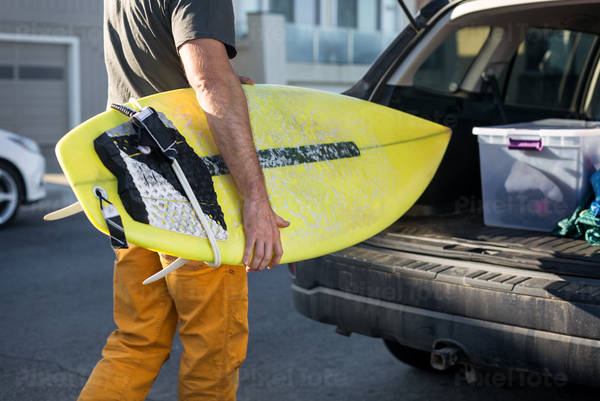 Male Surfer Unloading a Surfboard from a Car