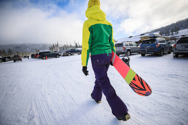 Woman Carrying a Snowboard at a Parking Lot of a Ski Resort