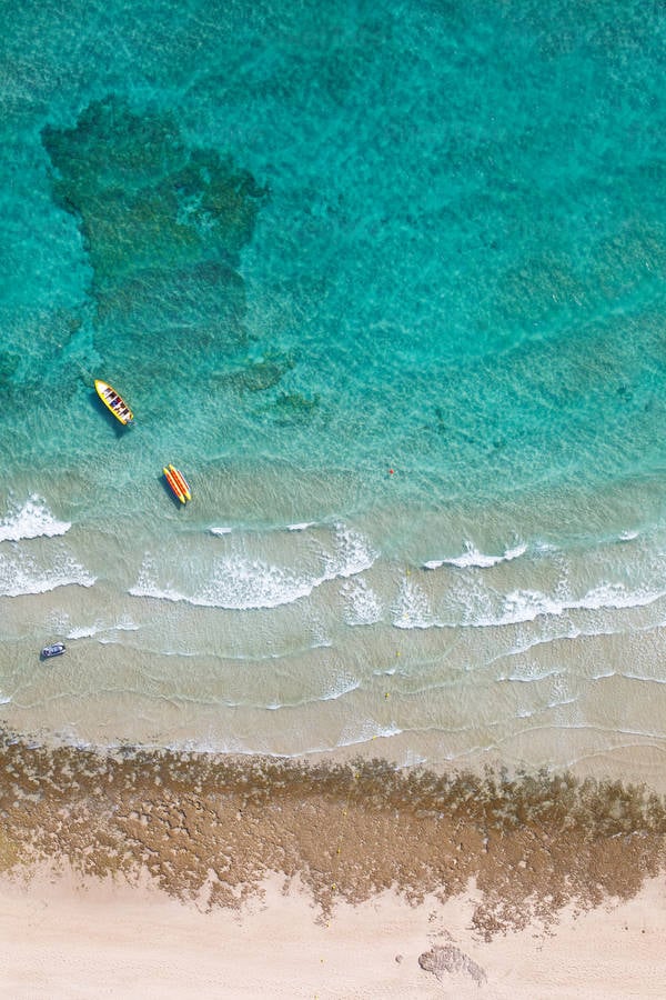 Aerial View of a Turquoise Sea Water with Boats and Waves Breaking
