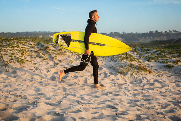 Male Surfer Running to a Beach While Carrying a Surfboard