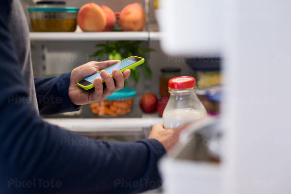 Man Looking at a Grocery Shopping List on a Cell Phone at a Refrigerator