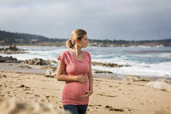 Pregnant Woman Holding Her Bump and Walking on a Beach