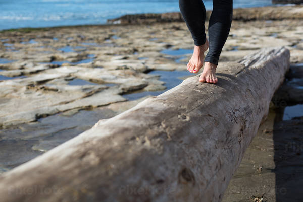 Low Section of a Woman Walking on a Tree Trunk on a Beach