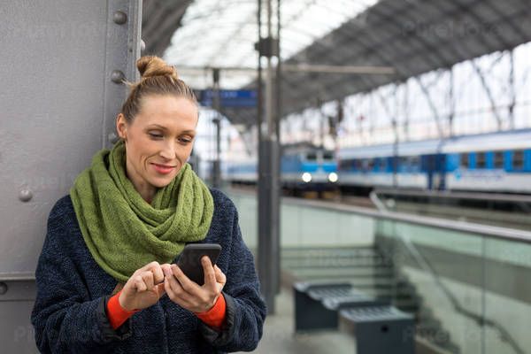 Smiling Woman Holding a Cell Phone in a Train Station