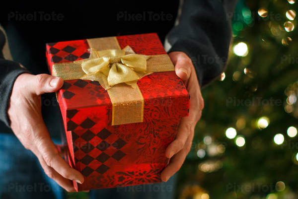 Man Holding Present in Front of a Christmas Tree