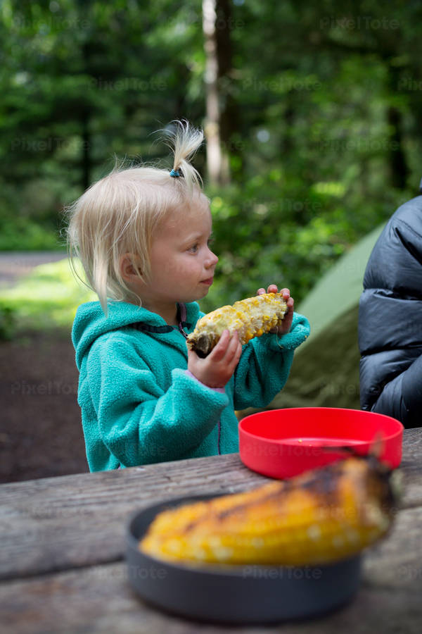 Toddler Girl Eating Corn on a Cob at a Campsite
