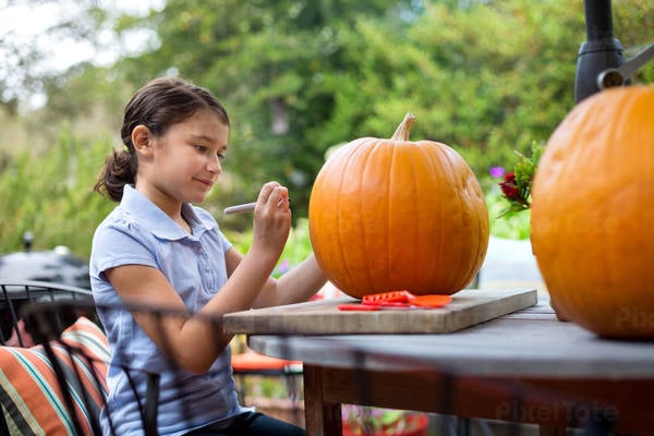 Smiling Young Girl Drawing on a Pumpkin on a Patio
