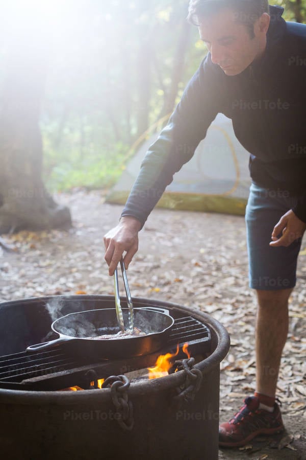Man Using Tongs to Cook Breakfast on an Outdoor Fire Pit