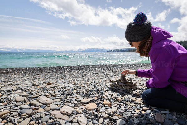 Woman Building a Cairn from Pebbles on a Shore of a Mountain Lake