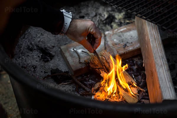 Man's Hand Starting Fire in a Fire Pit in Campground