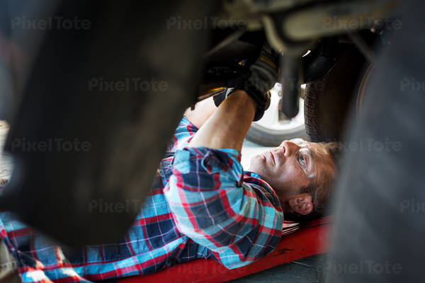 Auto Mechanic Laying on a Creeper Working Underneath the Front of a Car