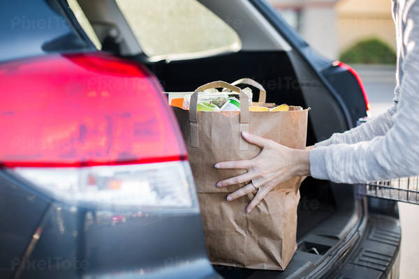 Woman Loading a Paper Bag with Groceries into a Hatchback Car