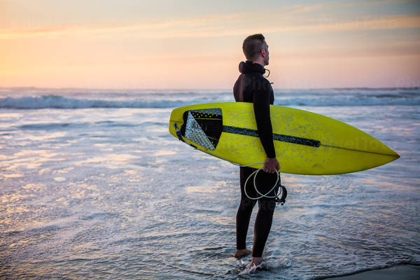 Male Surfer with a Surfboard Standing on a Beach During Sunset