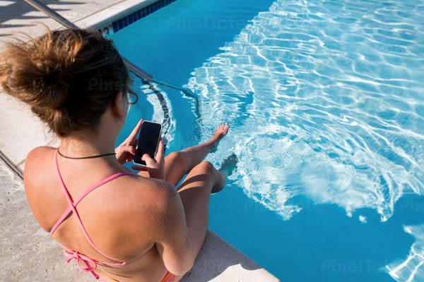 Woman Sitting by an Outdoor Pool and Browsing on a Smartphone