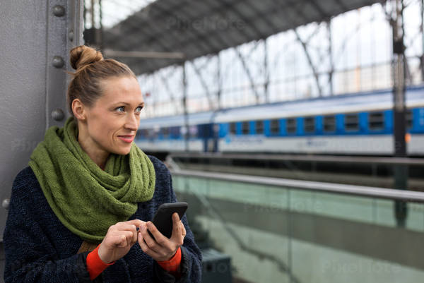 Smiling Woman Holding a Cell Phone on a Railroad Platform