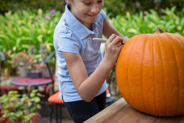 Smiling Young Girl Drawing on a Pumpkin