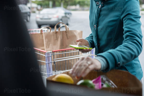 Woman Using a Cell Phone and Arranging Bag with Groceries in a Car