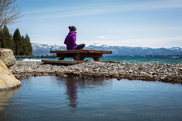 Woman in Winter Gear Sitting on an Alpine Lake Beach and Contemplating