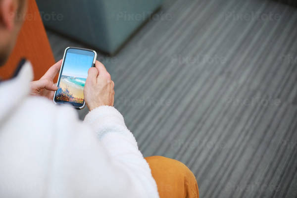 Over-The-Shoulder View of a Man Sitting down and Looking at His Cell Phone