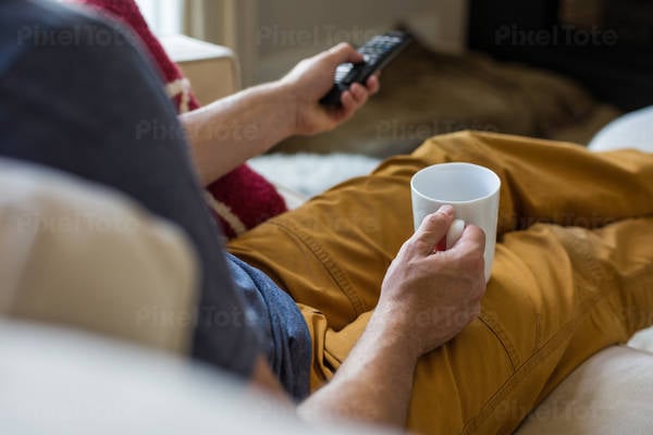 Man Holding a Coffee Cup and Using a TV Remote Control