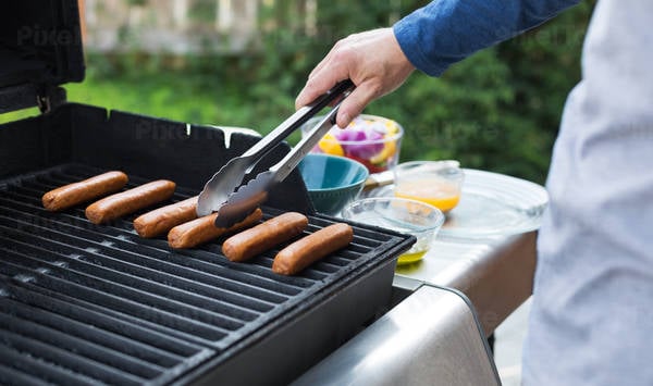 Man Grilling Sausages on a Barbecue in a Garden