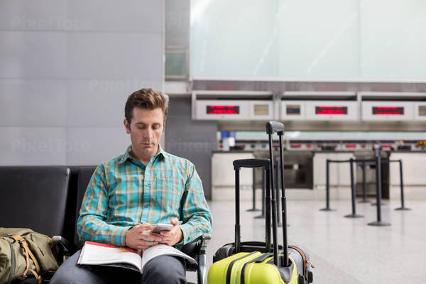 Traveler Sitting at an Airport Lobby Looking at a Cell Phone Waiting for His Flight