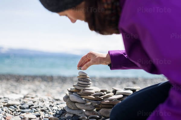 Woman Stacking up Pebbles on a Rocky Beach by an Alpine Lake