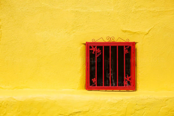 Window with a Red Ornamental Frame on a Mustard-Yellow Stucco Wall