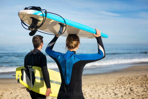 Two Surfers Walking on a Beach and Carrying Surfboards