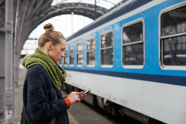 Woman with a Cell Phone Standing on a Train Station Platform