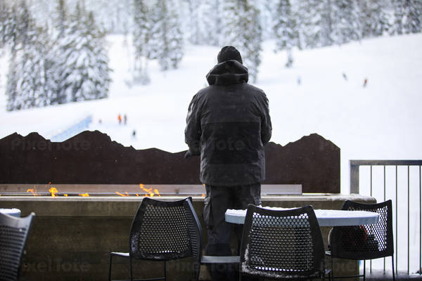 Back-View of a Man Warming His Hands Above the Flames at a Ski Resort
